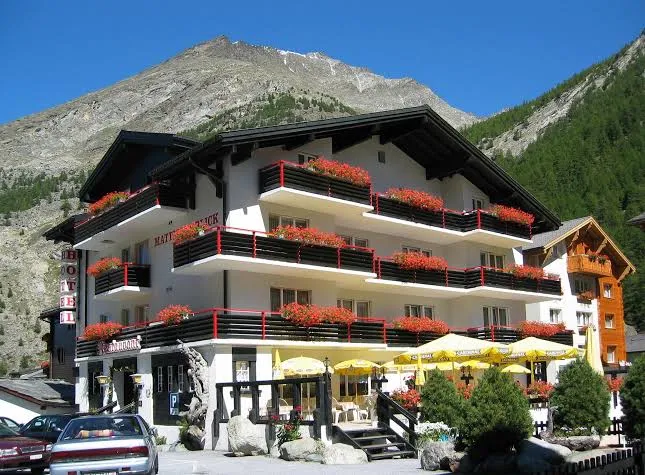 Exterior of Hotel Mattmarkblick with flower-lined balconies, restaurant terrace and alpine mountains behind